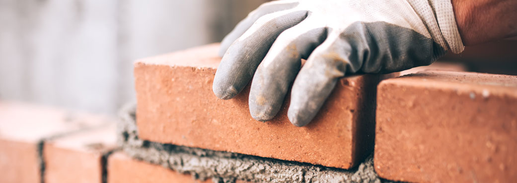 A gloved hand fixing bricks onto a wall