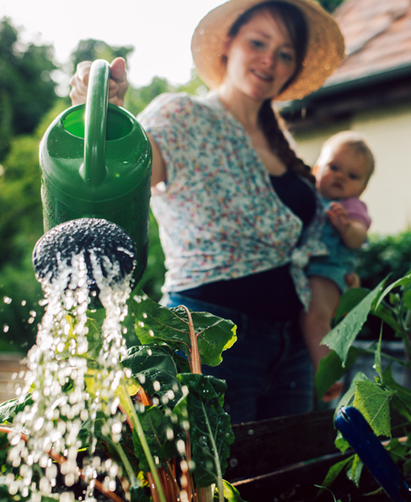 Woman holding a baby watering a plant in the garden